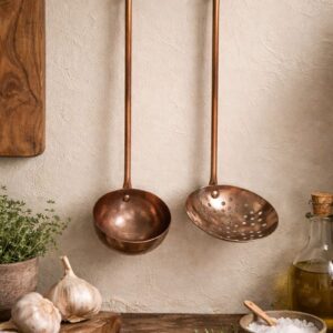 Vintage copper ladle and skimmer set hanging on a rustic wooden wall with aged patina