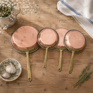 Set of vintage French copper frying pans with brass handles in graduated sizes displayed together as rustic kitchen décor
