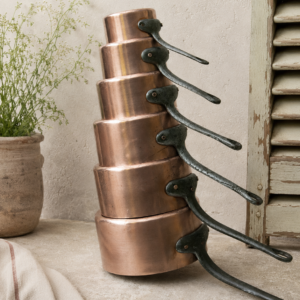 Vintage French copper saucepan set with six decorative copper pans and aged metal handles arranged together