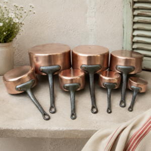 Vintage French copper saucepan set with seven decorative copper pans displayed in graduated sizes for French country kitchen decor