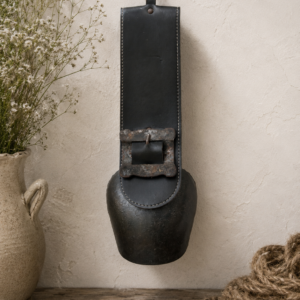 Vintage French cow bell with leather strap and forged metal body hanging as rustic farmhouse decor